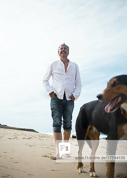 Glücklicher Mann geht mit Hund am Strand spazieren