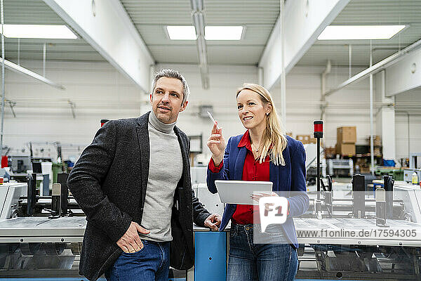 Smiling businesswoman holding tablet PC sharing ideas with colleague standing by machinery