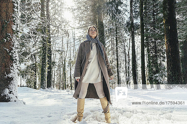 Frau in warmer Kleidung steht im tiefen Schnee im Wald