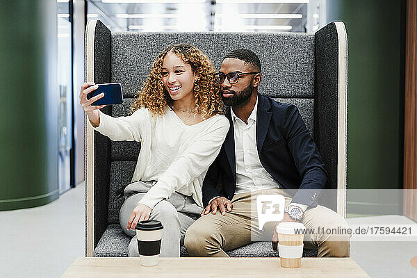 Business colleagues taking selfie sitting on seat at coffee break in coworking office
