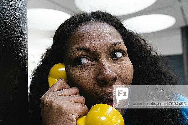 Curious woman listening through old-fashioned yellow telephone receiver