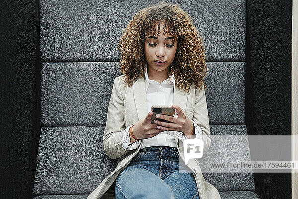 Young businesswoman with brown curly hair text messaging through smart phone in office