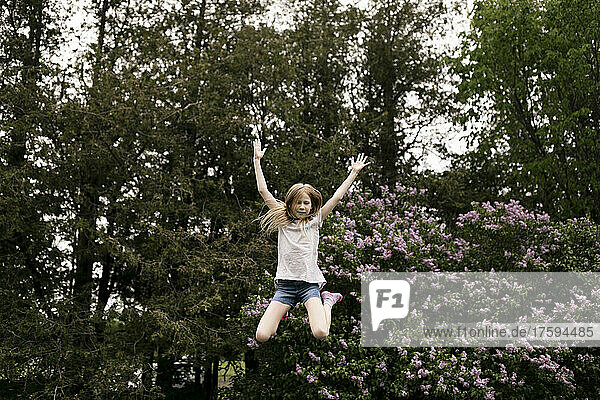 Fröhliches Mädchen springt vor lila Blumen in der Natur