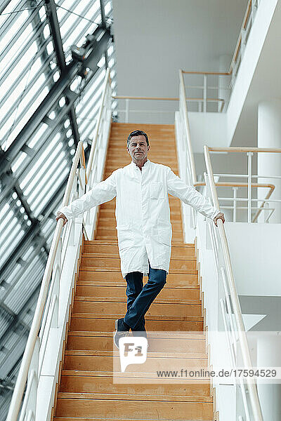 Scientist standing on staircase holding on railing at clinic