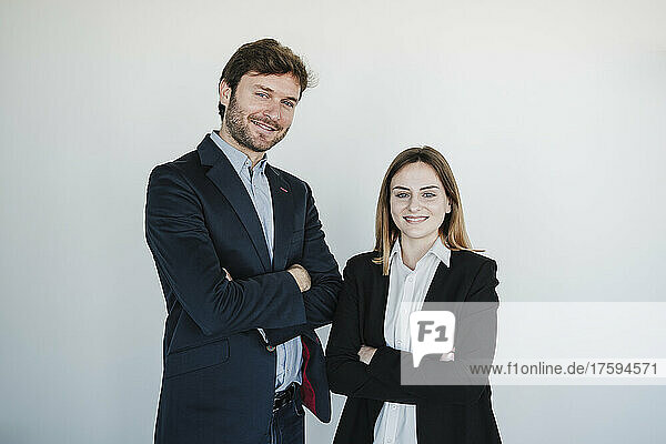 Smiling businessman and businesswoman standing with arms crossed in front of wall