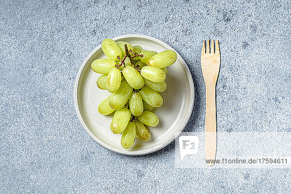 Studio shot of wooden fork and plate of ripe grapes