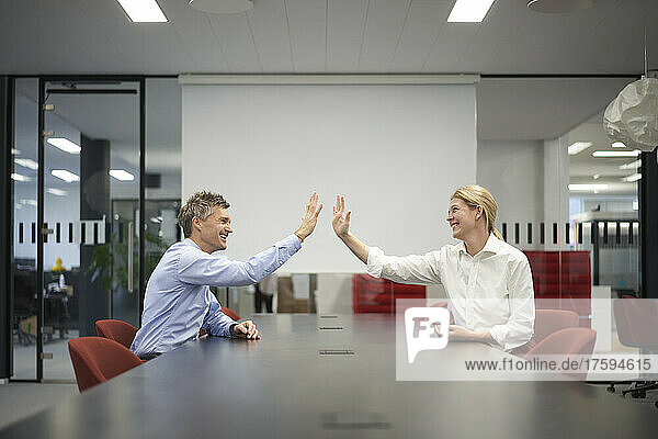 Smiling business colleagues giving high-five in meeting room
