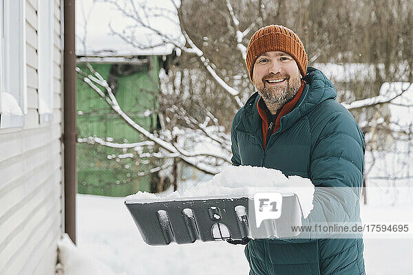 Smiling man holding snow shovel with snow in winter