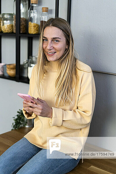Smiling woman with mobile phone in kitchen at home