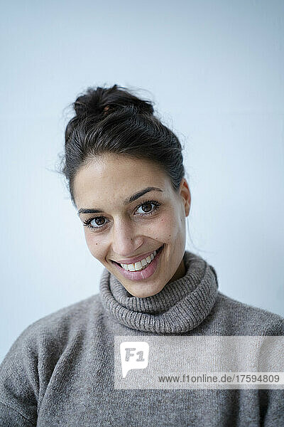 Woman wearing gray sweater smiling in front of wall
