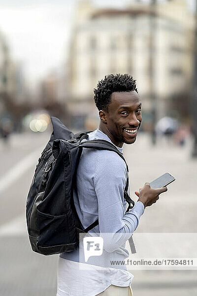 Smiling young man with backpack holding mobile phone