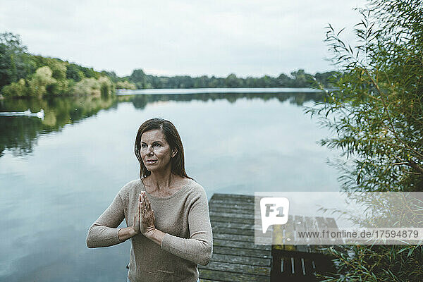 Frau mit gefalteten Händen steht auf Steg am See
