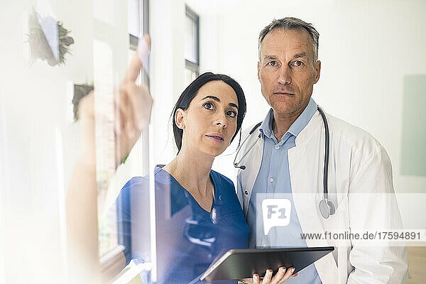 Krankenschwester hält Tablet-PC in der Hand und diskutiert mit Arzt im Krankenhaus