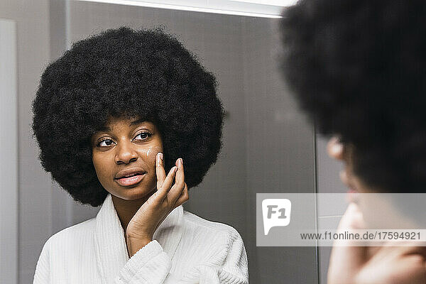 Afro-Frau trägt Gesichtscreme im Badezimmer auf
