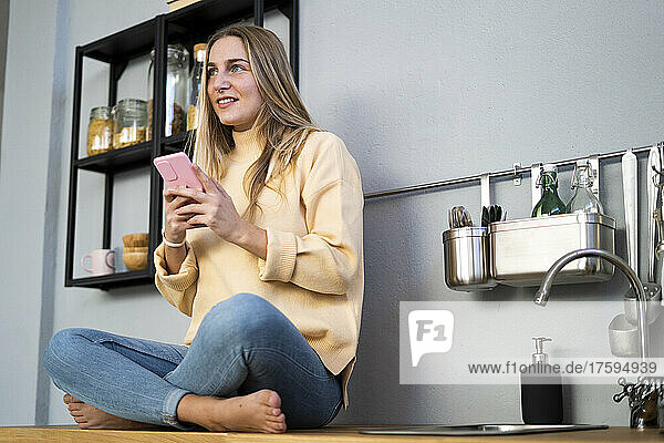 Contemplative woman with smart phone in kitchen
