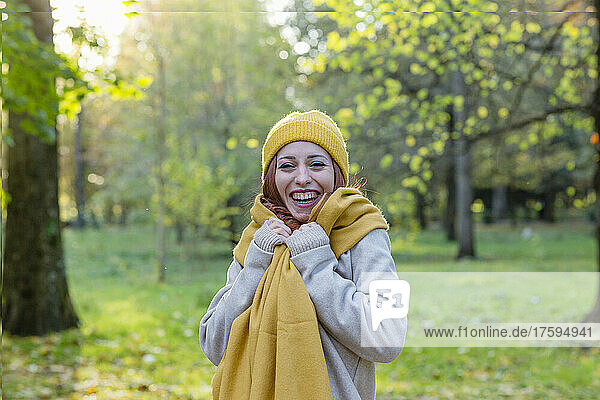 Fröhliche Frau mit gelber Strickmütze und Schal steht im Herbstpark