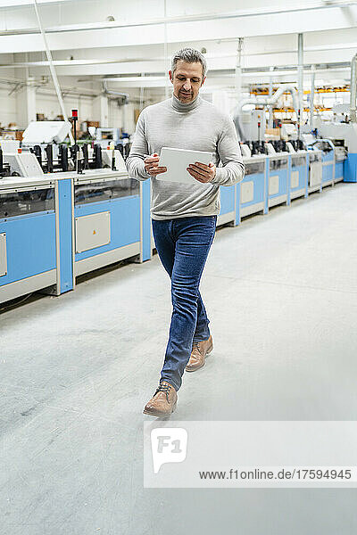 Businessman using tablet PC walking in production hall