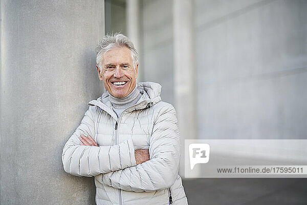 Happy senior man with arms crossed leaning on wall