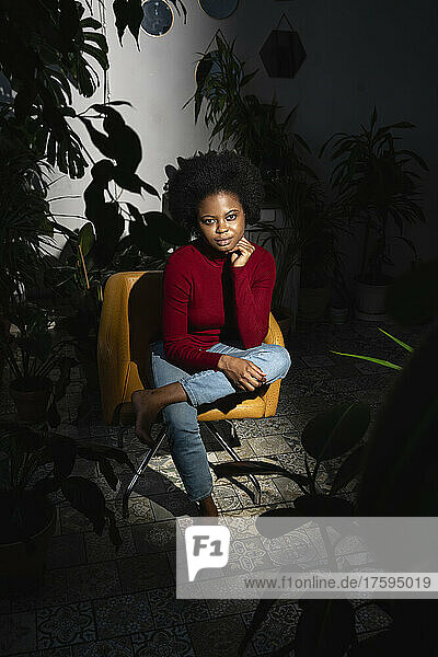 Young Afro woman on chair by plants at home