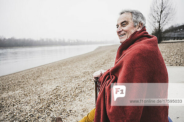 Happy man wrapped in blanket sitting at beach