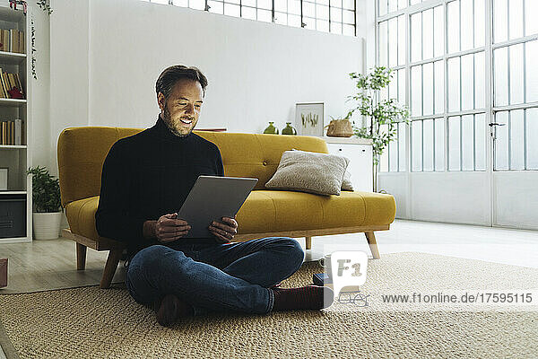 Mature man sitting on carpet using tablet PC at home