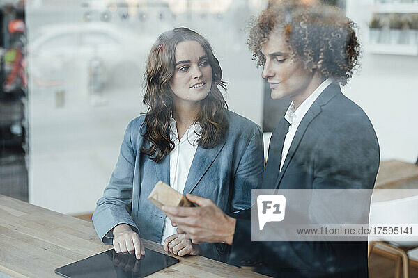 Businessman discussing over model house with businesswoman seen through glass window