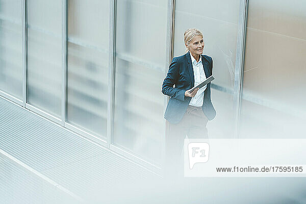 Contemplative businesswoman with tablet PC in office corridor