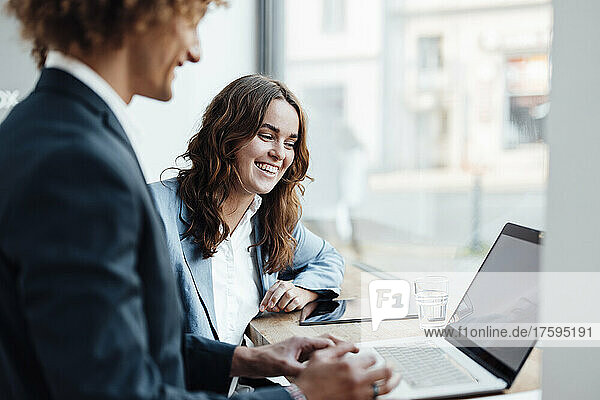Happy businesswoman discussing with colleague using laptop in coworking office