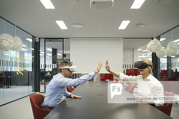Cheerful business people with VR glasses giving high-five in office