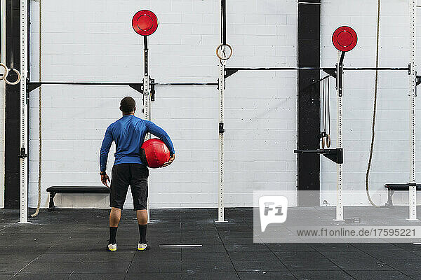 Athlete with medicine ball looking at exercise equipment in gym