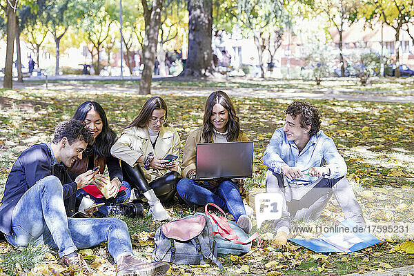 Zufriedene Studenten nutzen Smartphone und Laptop im College Park