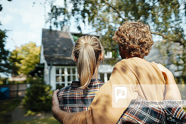 Couple with arms around looking at house