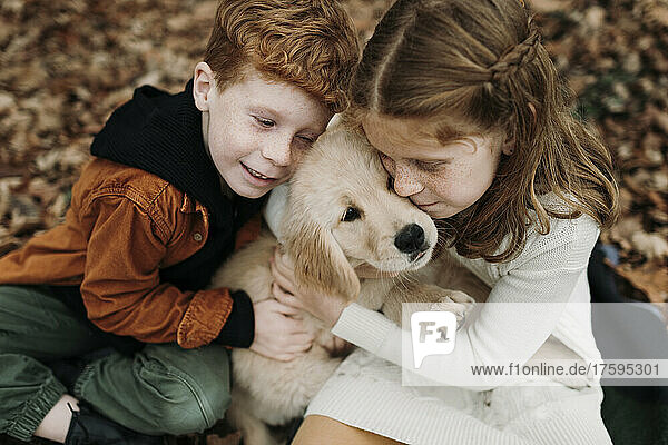 Siblings embracing golden retriever puppy in forest