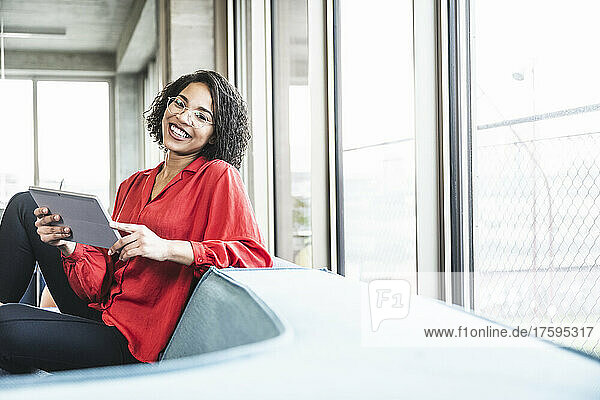 Smiling businesswoman with tablet PC sitting on sofa at work place