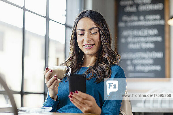 Young woman using smart phone and having cappuccino in cafe