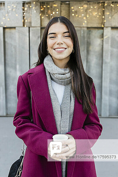 Lächelnde schöne junge Frau im Wintermantel mit Einwegbecher