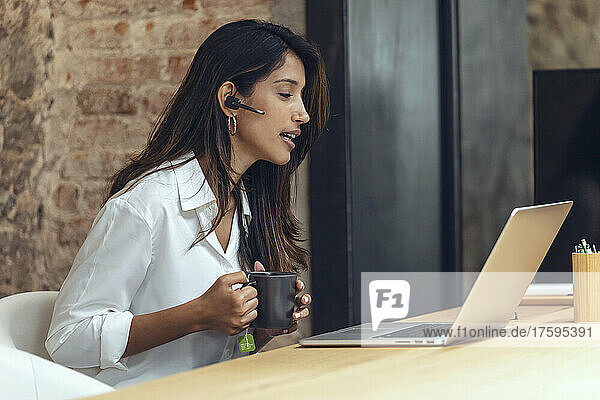 Businesswoman with coffee mug discussing on video call in coworking office