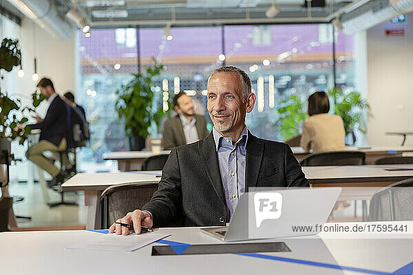 Smiling businessman with laptop at desk in coworking space