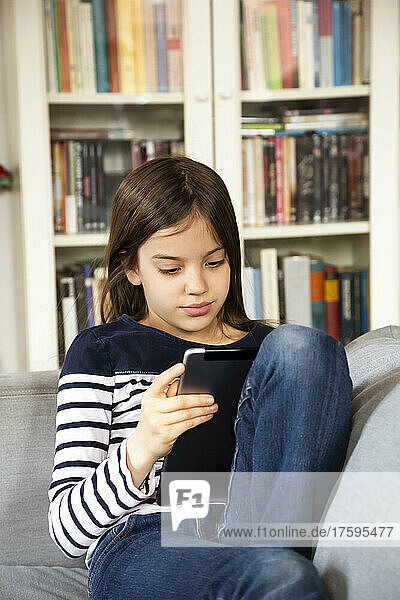 Young girl sitting on living room sofa with digital tablet in hands