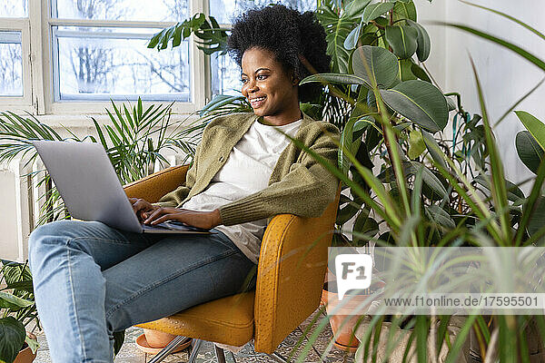 Smiling businesswoman working on laptop by plants at home