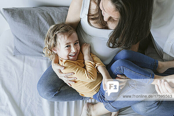 Cheerful girl lying on pregnant mother's lap at home