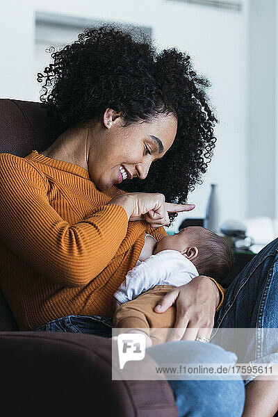 Mother breastfeeding baby boy in living room at home