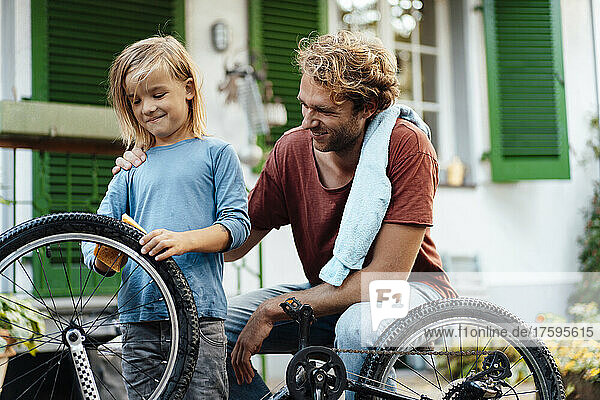 Smiling father looking at son cleaning bicycle outside house