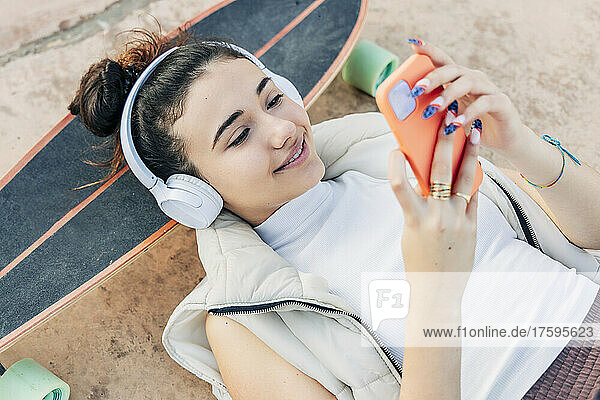 Woman with skateboard listening music on headphones and using smart phone