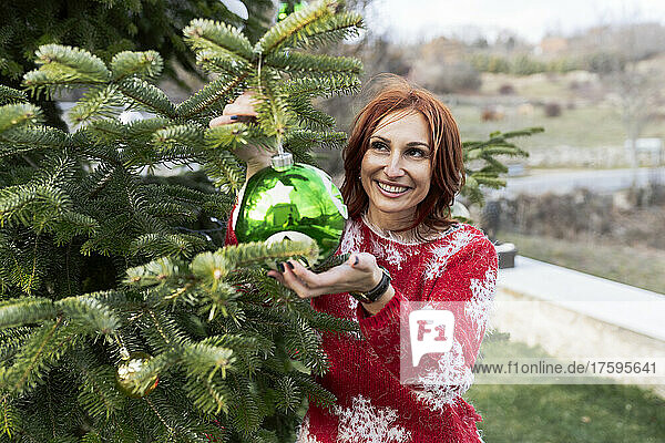Smiling woman hanging Christmas ornament on tree
