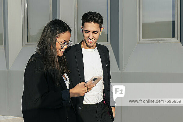 Smiling businesswoman sharing smart phone with colleague