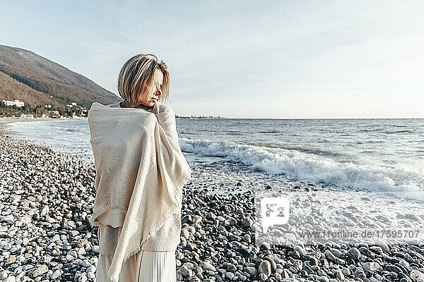 Blonde Frau in Decke gehüllt am Strand