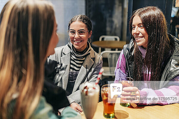 Smiling women talking with young friend in cafe