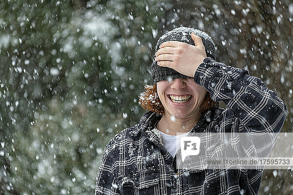 Cheerful man covering eyes with knit hat in snowfall