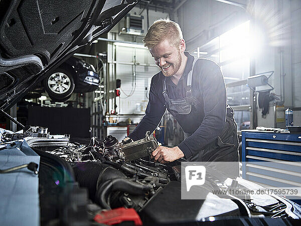 Smiling blond mechanic repairing car engine in auto shop